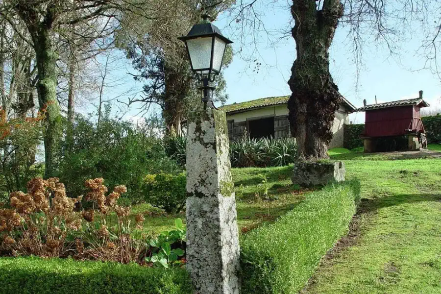 Tuin met stenen lantaarn, bijgebouw en Galicische hórreo op de achtergrond.